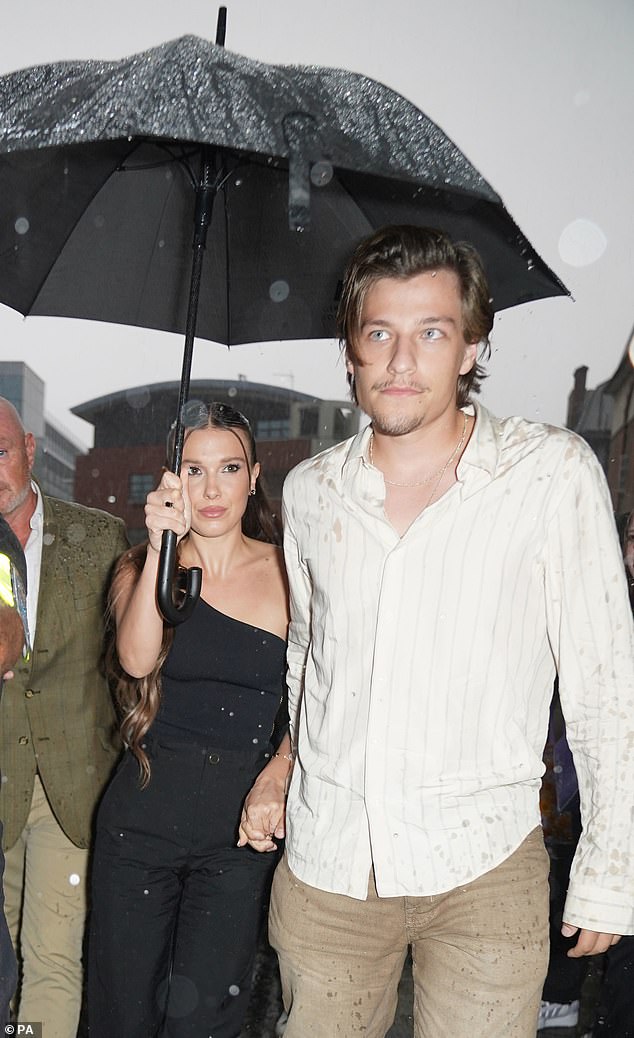 Taking cover: The actress, 19, and her fiance, Jon Bon Jovi's son, 21, did their best to take cover from the rain and stayed close under an umbrella as they entered the Hackney Empire in London