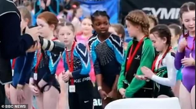 The little girl (center) shuffles forward excitedly as she awaits the medal presentation before the referee moves on to the next gymnast in the lineup