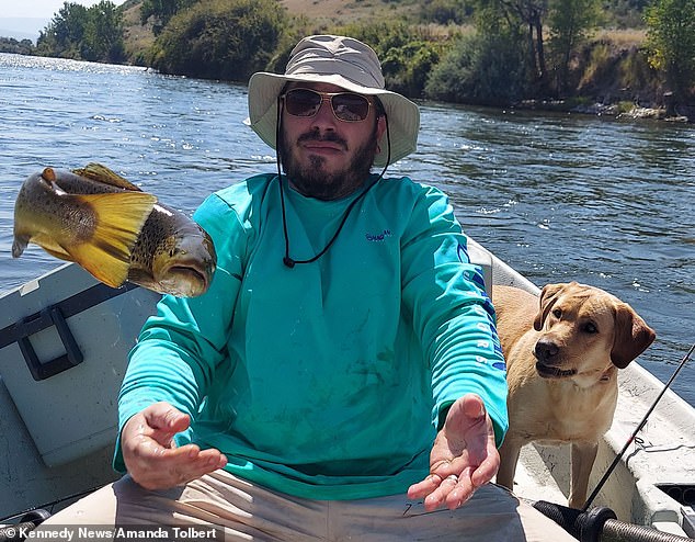 This is the hilarious moment a lively fish braved a daring escape and leapt into the air after being caught by a fisherman on Montana's Bighorn River.  (Image: Mike Wickham, 40, his one-year-old Labrador Cody and the lively fish)