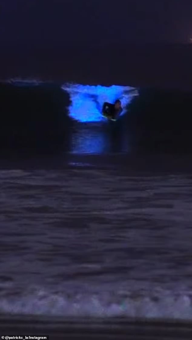 A photographer has captured bioluminescent plankton lighting a California beach with a bright blue glow as boogie boarders ride the waves