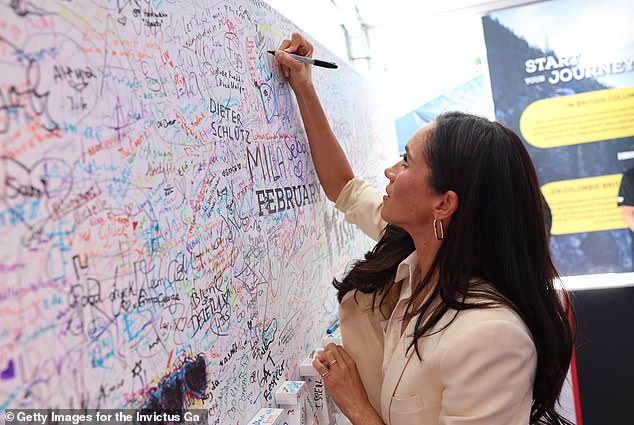 On day six of the Invictus Games, Meghan Markle writes her signature on a huge tribute wall full of names