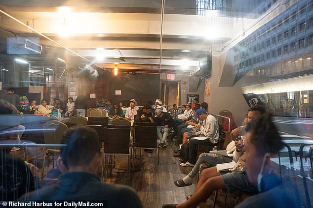 Migrants wait in a closed downtown bar attached to the Roosevelt Hotel as they are processed Monday