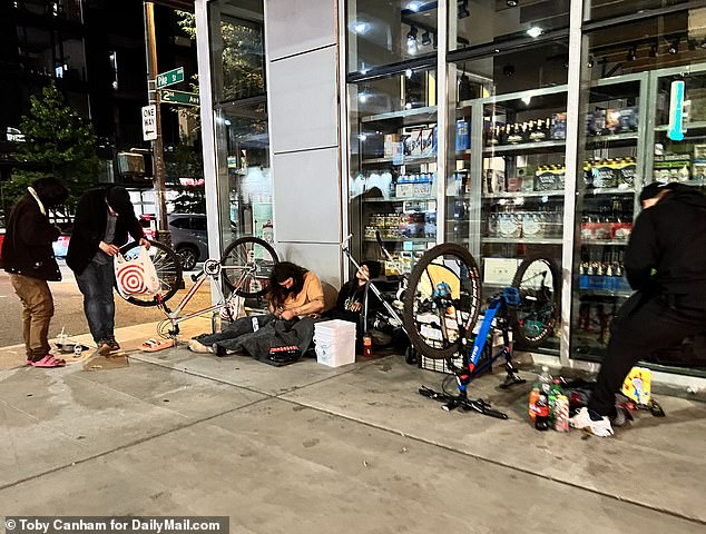 A man can be seen here openly using a hypodermic needle while lying on the sidewalk.