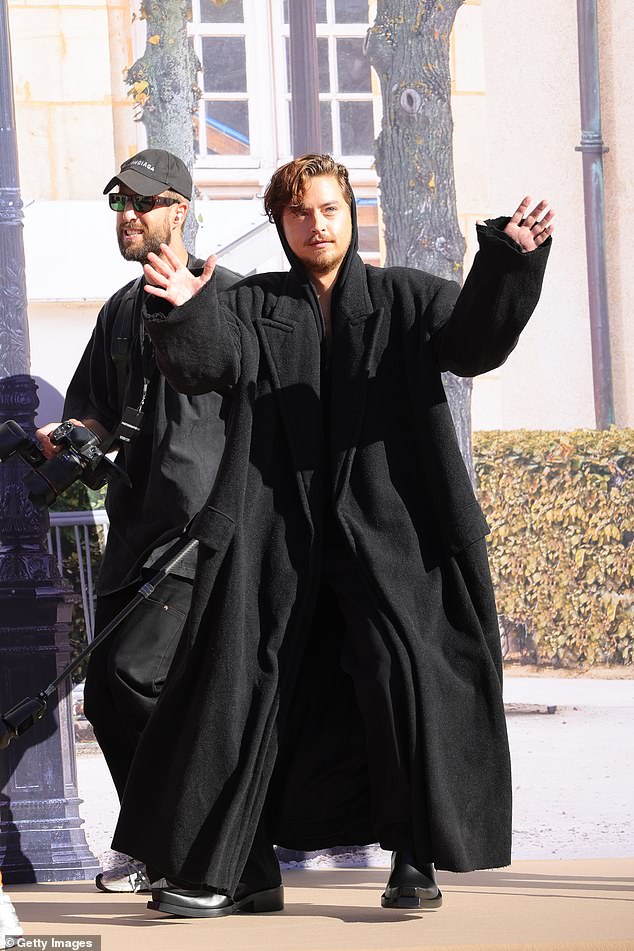 Stylish: Dylan Sprouse wore a long black trench coat with his hood up