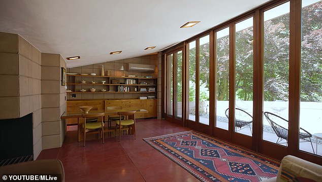 A floor-to-ceiling glass facade opens onto a terrace overlooking a meadow