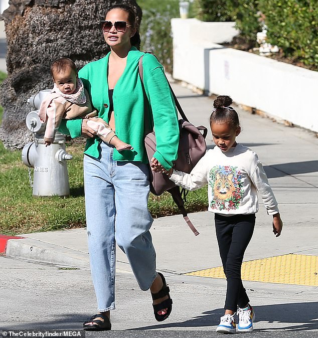 Staying warm: Teigen wore a bright green cardigan sweater on top of a low-cut black bra top as she spent time with her loved ones