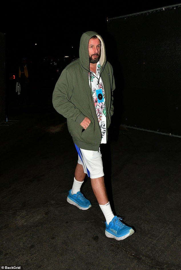 Adam Sandler wore an olive green hooded jacket over a Hawaiian shirt with athletic shorts and blue sneakers