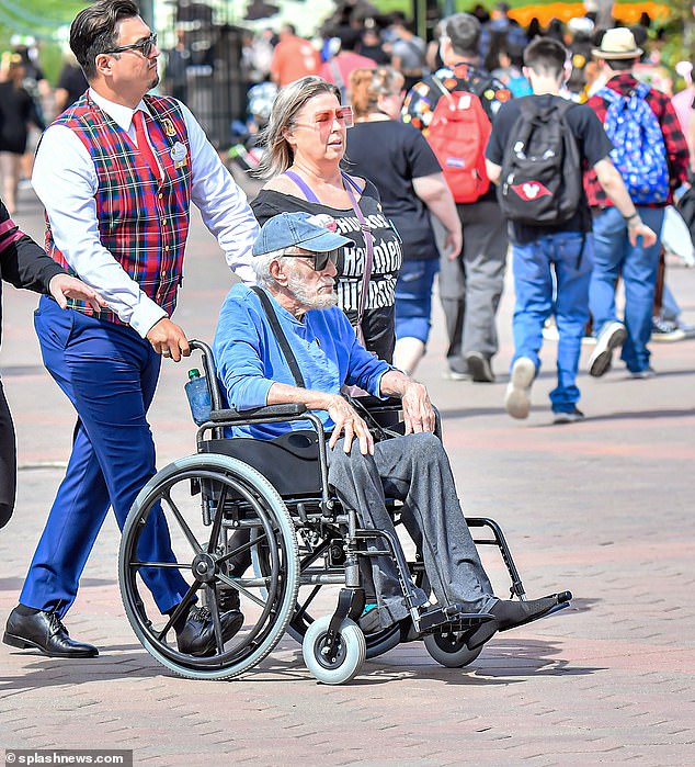 Day out: The acting icon - who revealed he recently learned the ukulele - looked in good spirits as he visited the theme park with his wife of 11 years - with a guide driving his wheelchair