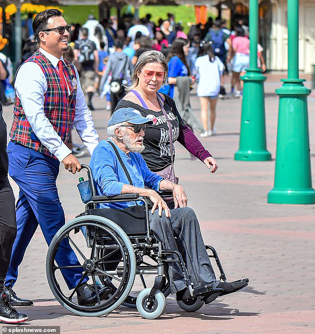 By his side: His wife wore a black haunted house top and matching pants, paired with tinted shades.