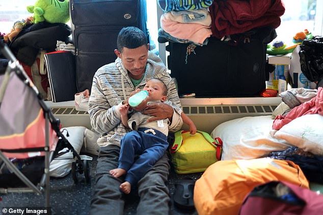 A migrant father from Venezuela feeds his 15-month-old son in the lobby of a police station