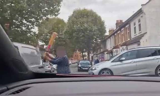 As it drives past him, the man swings the bat and makes contact with the rear sliding door