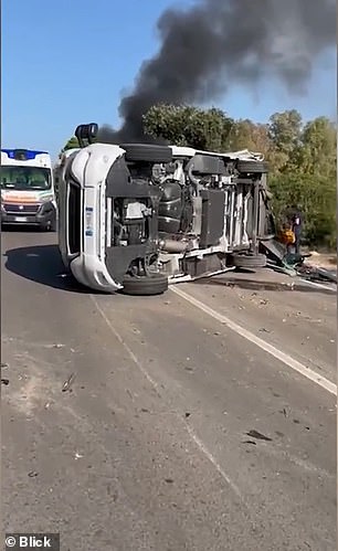 People have gathered next to the wrecked Lamborghini and overturned camper as black smoke billows from the flaming Ferrari, while an ambulance crew is also on the scene