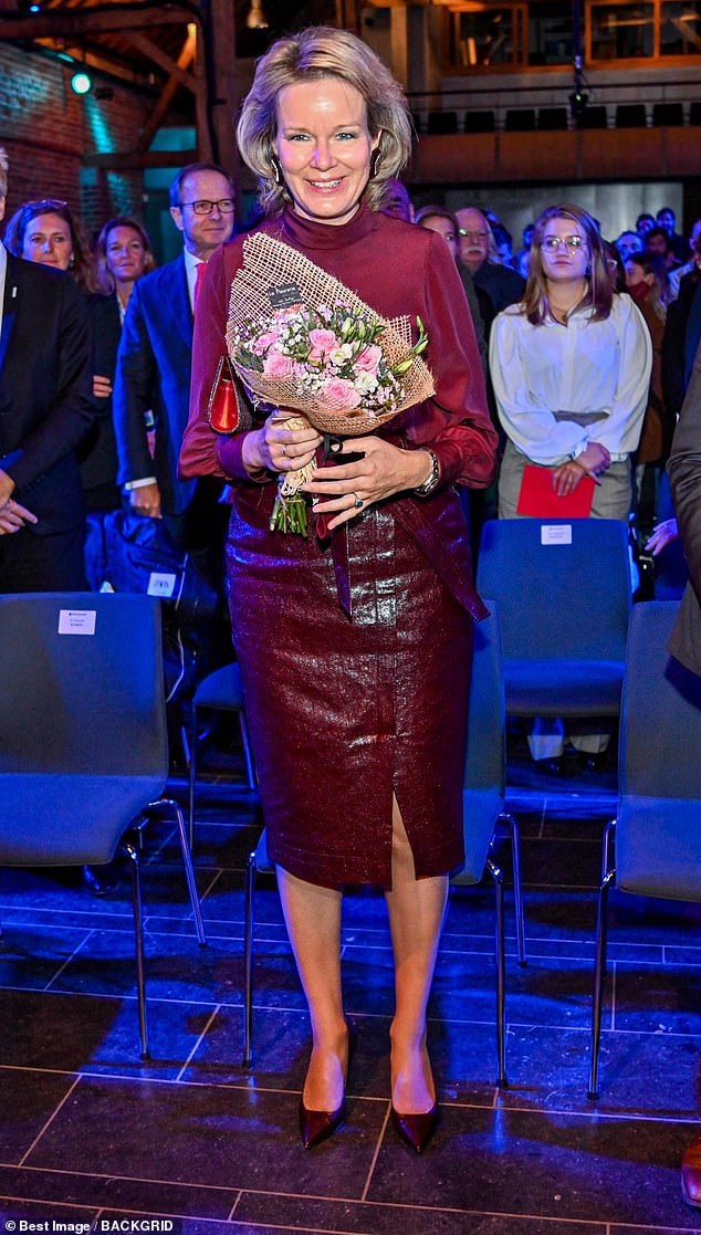 Queen Mathilde in a burgundy leather skirt and matching silk top at a conference in Belgium in 2021