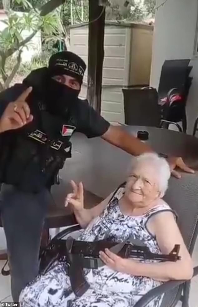 Another image shows a woman, who is being held hostage, holding a gun and raising her hands in a peace sign with a member of Hamas in a balaclava.