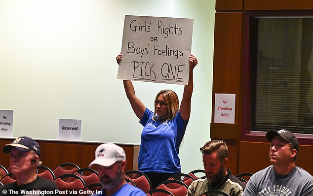 A woman holds a sign as Loudoun County School Board members vote to enact Policy 8040 amid protests over the two sexual assaults in 2021