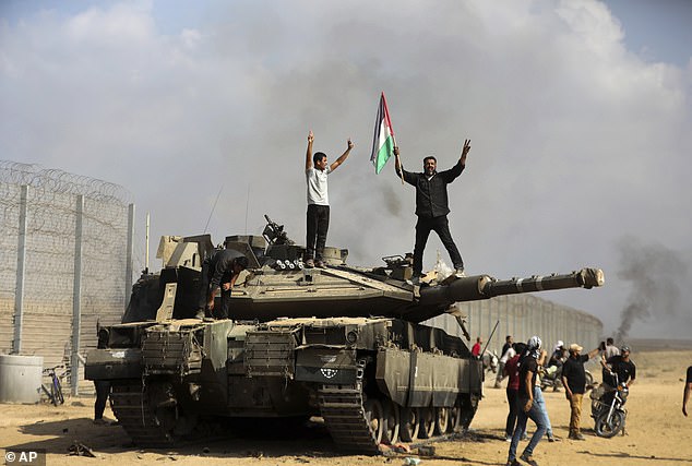Palestinians wave their national flag and celebrate by a destroyed Israeli tank at the Gaza Strip fence east of Khan Younis in southern Saturday, October 7, 2023