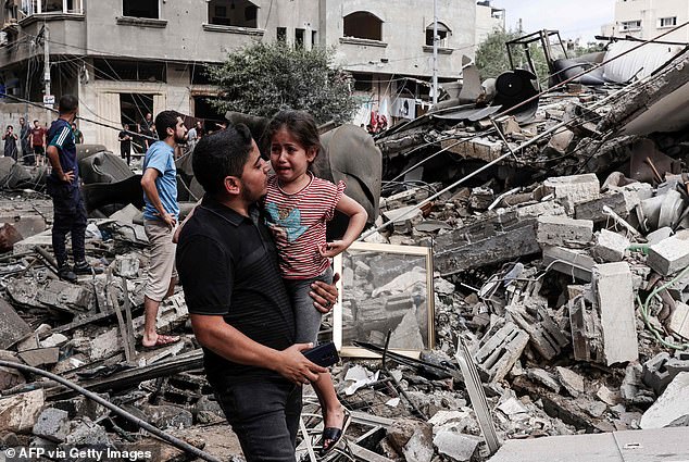 A crying child in her father's arms stands in front of a building destroyed by an Israeli airstrike in Gaza City early Saturday morning