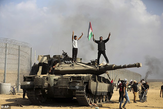 Palestinians wave their national flag and celebrate by a destroyed Israeli tank at the Gaza Strip fence east of Khan Younis south Saturday, October 7, 2023