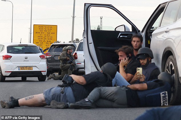 Journalists take cover behind cars as Israeli soldiers take up positions during clashes with Palestinian fighters near the Gevim kibbutz