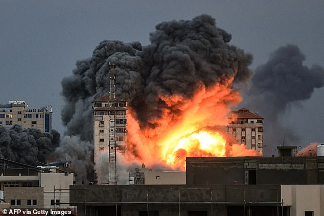 People standing on a rooftop watch a ball of fire and smoke rise above a building in Gaza City on Saturday