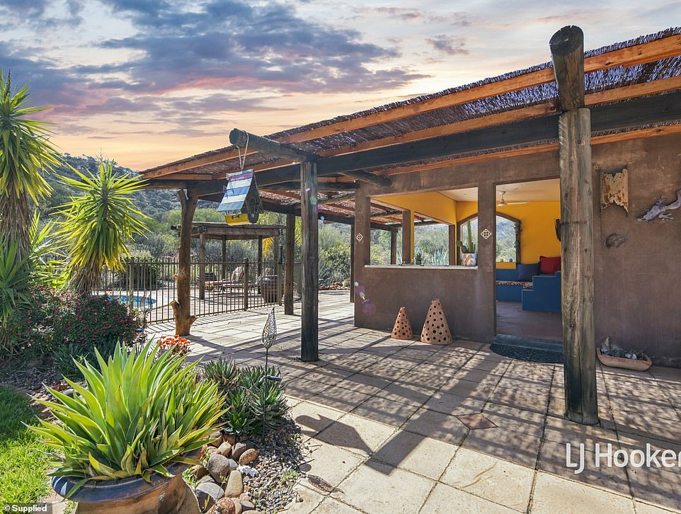 Bi-fold glass doors open to the entertainer's backyard with a heated pool and a vibrant cobalt blue and sunny yellow outdoor kitchen that has built-in seating all with Mexican touches like a chiminea and wood pergola by the pool