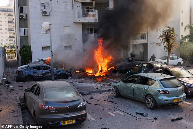 A member of the Israeli security forces stands near burning cars after a rocket attack from the Gaza Strip in Ashkelon, southern Israel