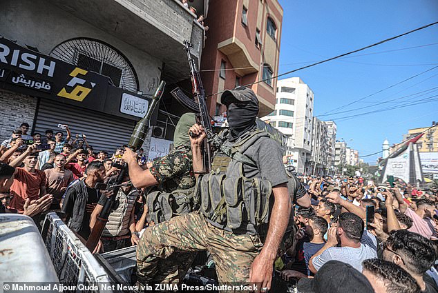 Palestinian militants swing their weapons as they drive through Israeli territory in trucks