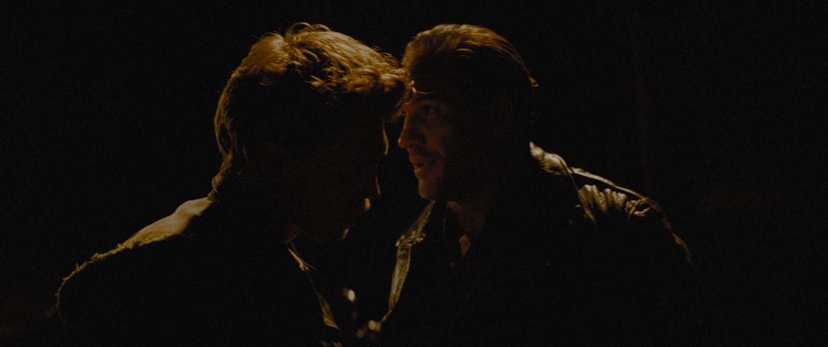 Austin Butler and Tom Hardy have an intense conversation, backlit and silhouetted in the dark in The Bikeriders