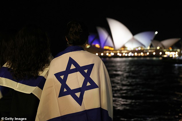 People watch as the colors of the Israeli flag are projected onto the Sydney Opera House