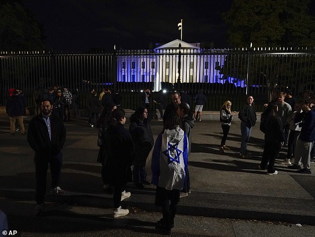 People stand with an Israeli flag outside the White House, which was lit up in blue and white on Monday night