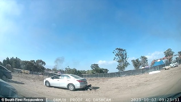 With the coast seemingly clear, another festival-goer pretending to be dead behind a car briefly raises his head to check his surroundings.