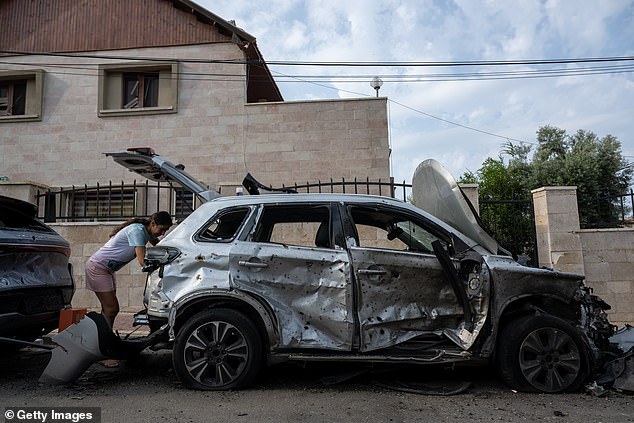 A woman goes through the trunk of her car after it was hit by a rocket the day before on October 10, 2023 in Ashkelon, Israel