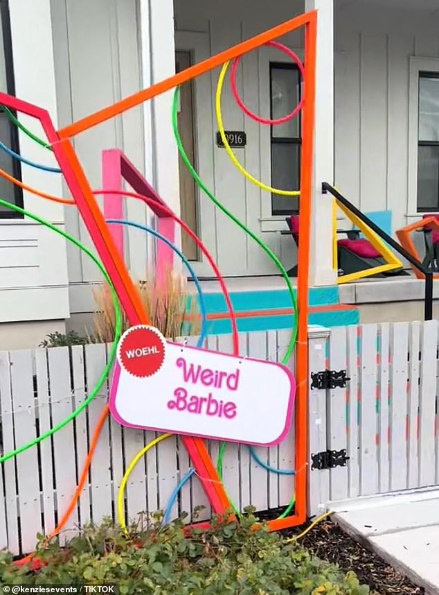 Weird Barbie's house has neon-colored 2D and 3D metal shapes attached to the picket fence and porch, a nod to the character's appearance in the movie