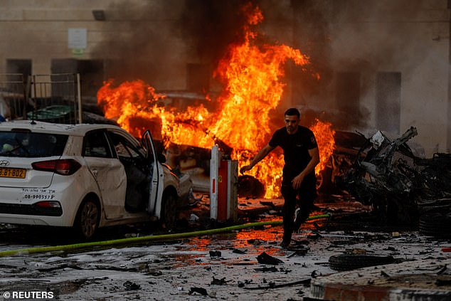 A man runs on a road as fire burns after rockets were launched from the Gaza Strip, in Ashkelon, Israel