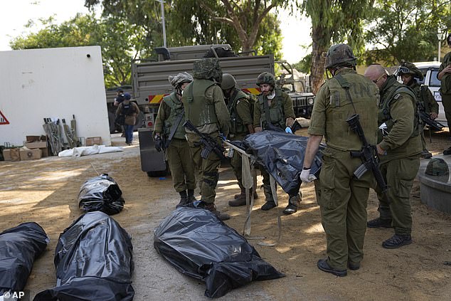 Israeli soldiers carry the body of a person killed by Hamas militants in Kibbutz Kfar Azza on Tuesday, October 10, 2023