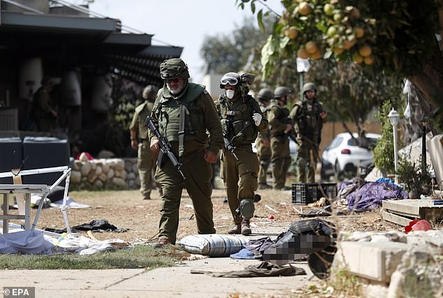 Israeli soldiers walk next to the bodies of Hamas militant killed in Kfar Aza kibbutz on Tuesday