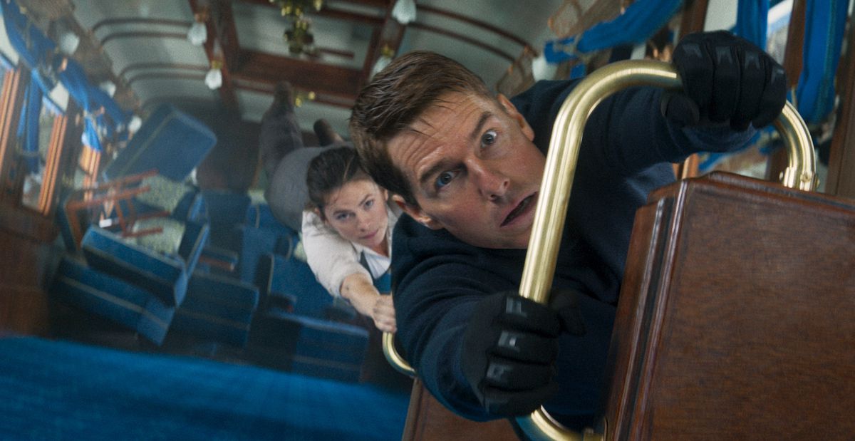 Tom Cruise as Ethan Hunt holds onto a railing in a vertically turned train car as Hayley Atwell clings to him in Mission: Impossible – Dead Reckoning Part One