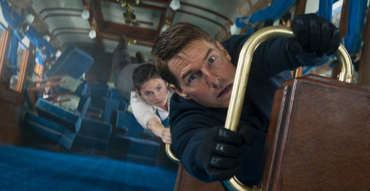 Tom Cruise as Ethan Hunt is holding on to a car that is facing a direct attack, as Hayley Atwell is holding on to him in Mission: Impossible - Fallout Part One