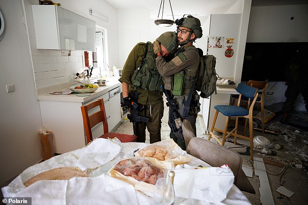 An Israeli soldier breaks down in tears at the sight of a family dining table that still has Challah bread from Friday's Kiddush at Kibbutz Kfar Aza.  Hamas terrorists massacred families here on Saturday