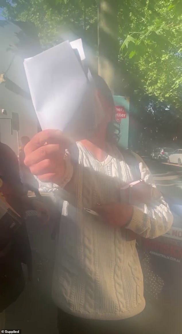 The man tried to shield his face from the camera with a piece of white paper (pictured) while Ms d'Abrera recorded the man's tirade on her phone