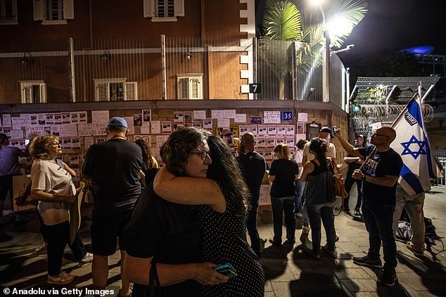 People hug as others look at photos of Hamas kidnapping victims on a wall outside the Israeli Ministry of Defense in Tel Aviv