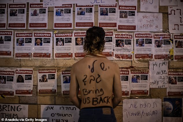 A protester with a painted message reading 'bring us back' looks at photos of Hamas kidnap victims at the site of the anti-Netanyahu protest