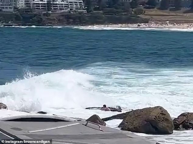 Beachgoers watch as the man is battered by the surf and smashed against the rocks