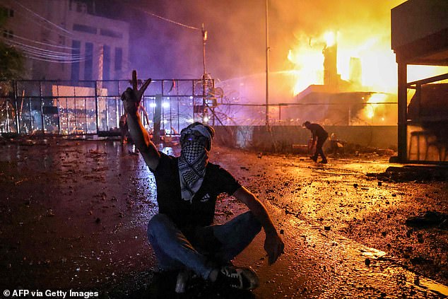 A Lebanese protester is seen as a fire rages behind the security gate of the US Embassy after clashes with security forces in Beirut on October 18