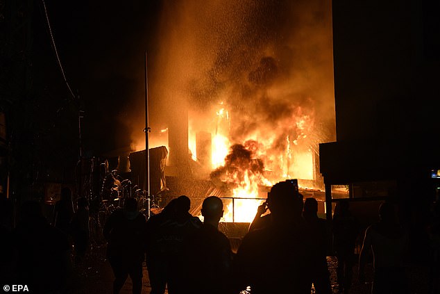 People stand in front of the fire that broke out outside the security gate, during clashes between protesters and security forces outside the US Embassy in Beirut, Lebanon