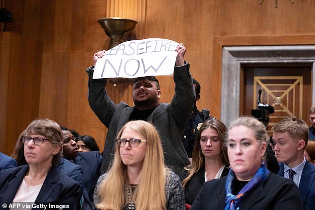 Holding a sign reading “ceasefire now,” the protester shouted: This is not the time to play political games.  How many bombs need to be dropped?  How many children should be killed?  Our families are dying.”