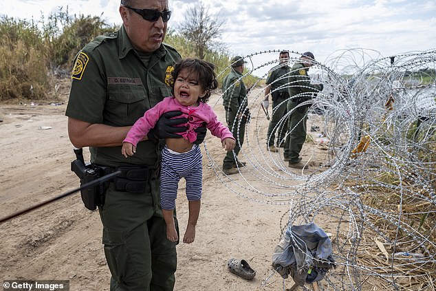 A U.S. Border Patrol agent detains a child from Venezuela as her parents pass through barbed wire at the U.S.-Mexico border in Eagle Pass, Texas, on September 27