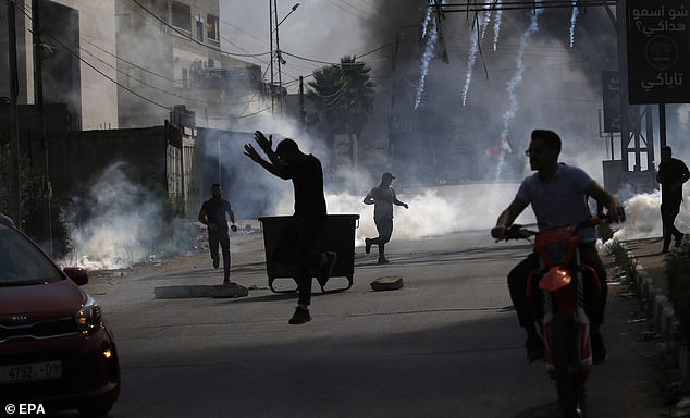 Palestinians take cover as tear gas canisters fall during clashes with Israeli forces in the West Bank city of Nablus, October 13, 2023