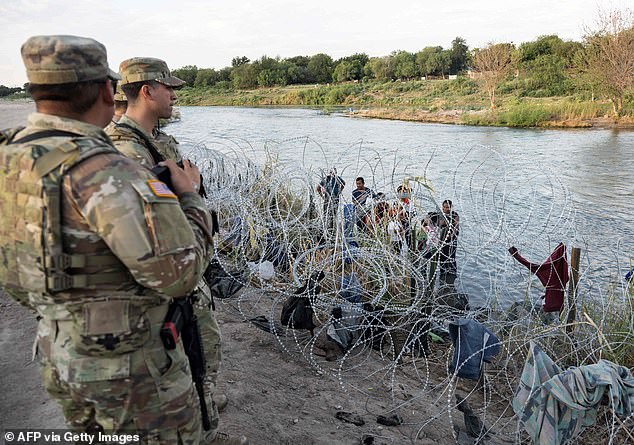 National Guard members watch as migrants try to find their way past barbed wire in Eagle Pass, Texas