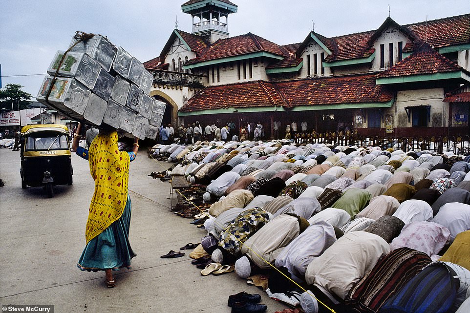 A woman carrying metal boxes walks past hundreds of men in prayer at the Bandra train station in Mumbai, India, in this 1996 photo